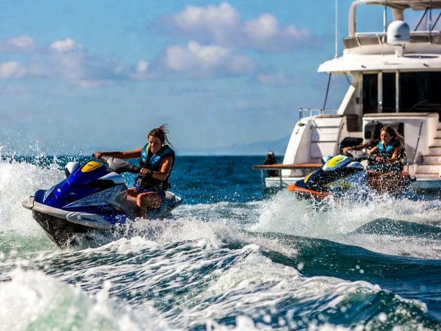 Two riders in life jackets launching jet skis off the back of a yacht
